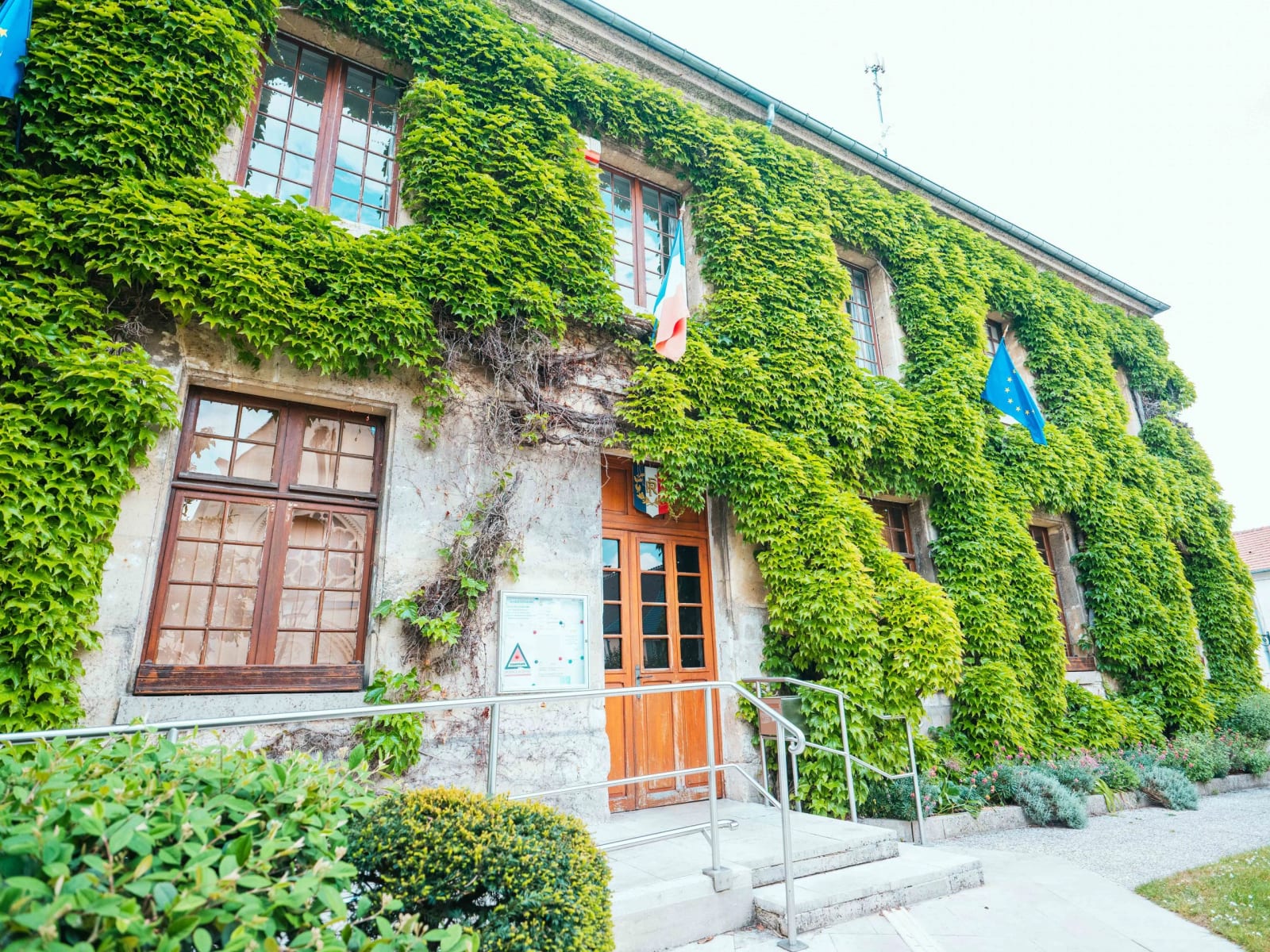 La façade de la mairie couverte de lierre, drapeaux français et européen, avant la cérémonie civile, mariage au Domaine la Ferme du Roy, par Jean-Baptiste Argyre (Jaysphotography)