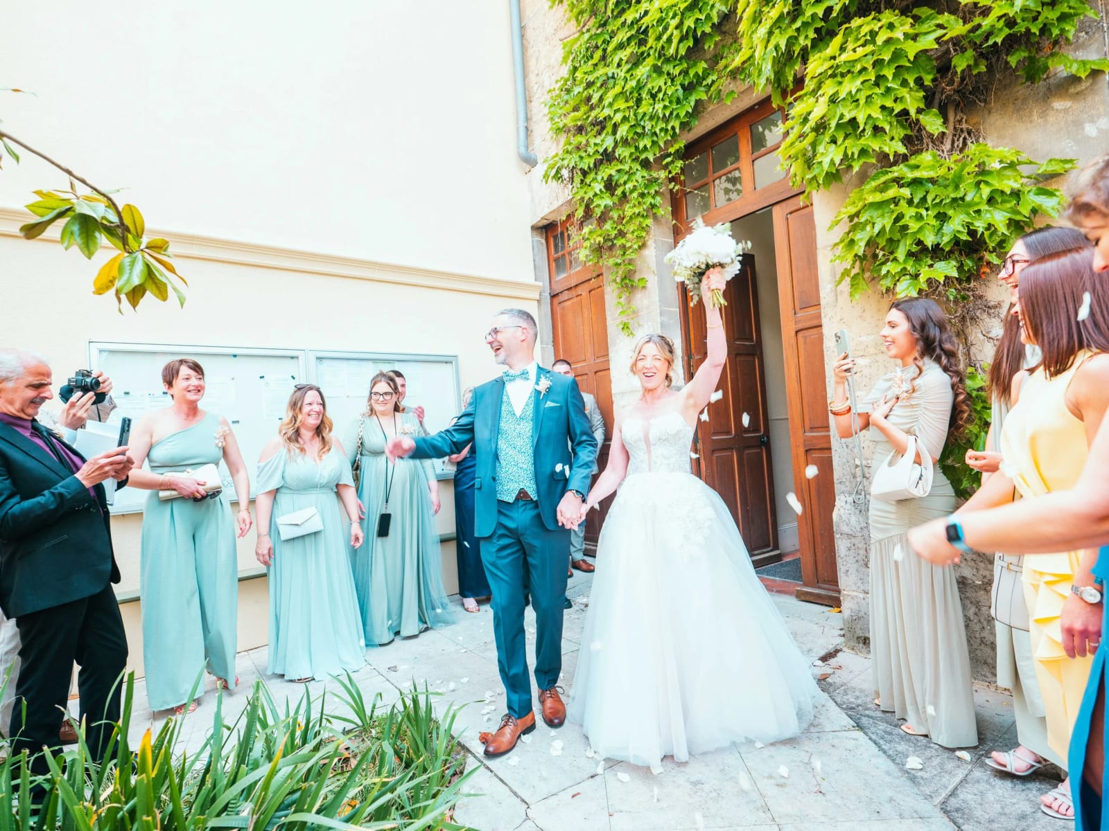 Lydia et Éric sortent sous une pluie de pétales, demoiselles d'honneur en vert sauge, mariage au Domaine la Ferme du Roy, par Jean-Baptiste Argyre (Jaysphotography)