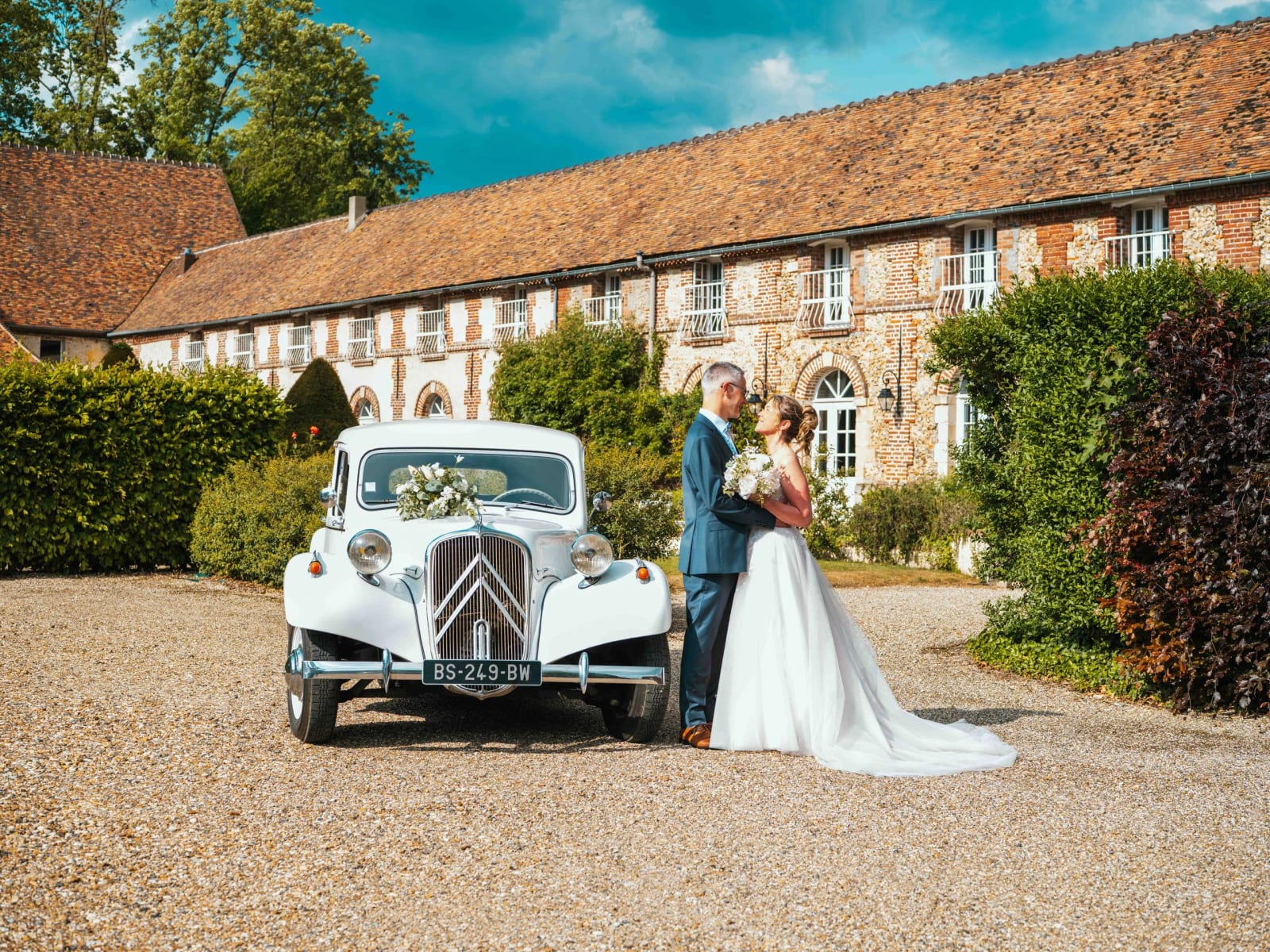 Lydia et Éric s'embrassent devant une Citroën Traction blanche sur l'allée du domaine, mariage au Domaine la Ferme du Roy, par Jean-Baptiste Argyre (Jaysphotography)