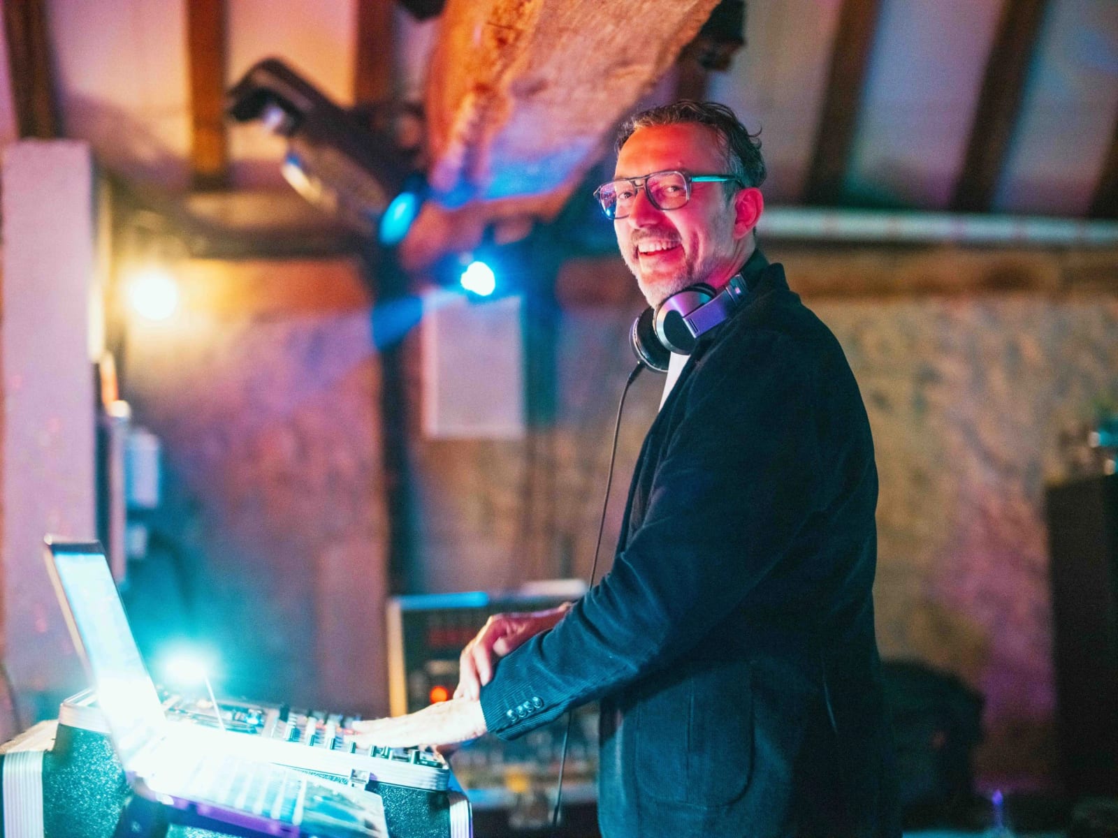 Le DJ derrière sa console sous les lumières colorées de la grange, mariage au Domaine la Ferme du Roy, par Jean-Baptiste Argyre (Jaysphotography)
