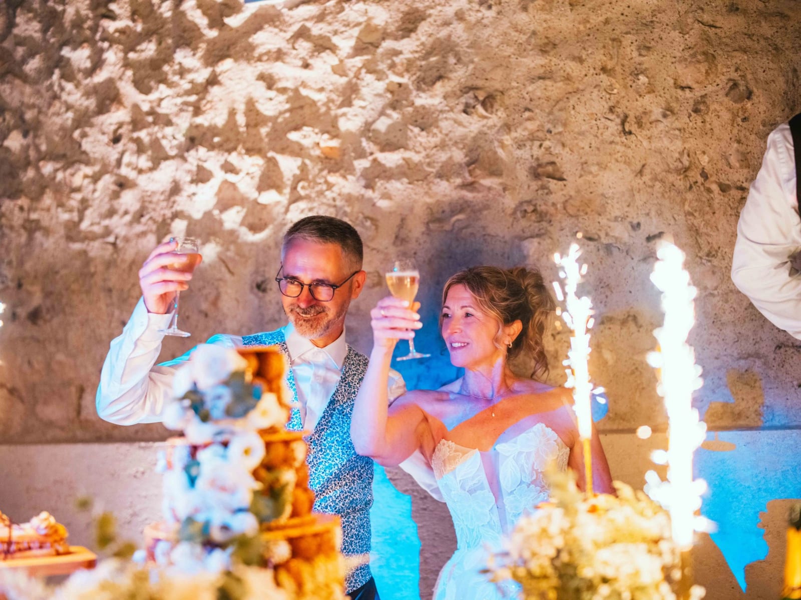 Lydia et Éric portent un toast au champagne devant le gâteau et les fontaines d'étincelles, mariage au Domaine la Ferme du Roy, par Jean-Baptiste Argyre (Jaysphotography)