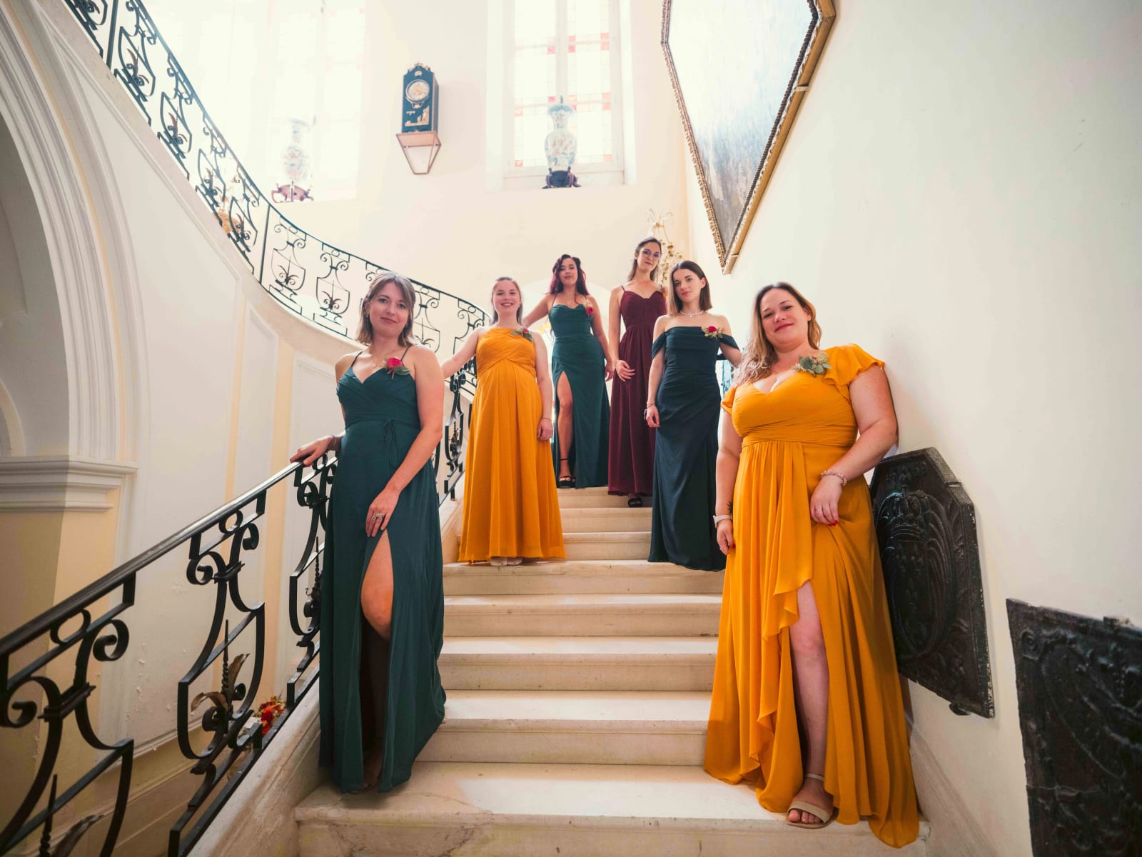 Sept demoiselles d'honneur en robes vert bouteille, moutarde et bordeaux sur le grand escalier de pierre à rampe en fer forgé, mariage à l'Abbaye de Longpont, par Jean-Baptiste Argyre (Jaysphotography)