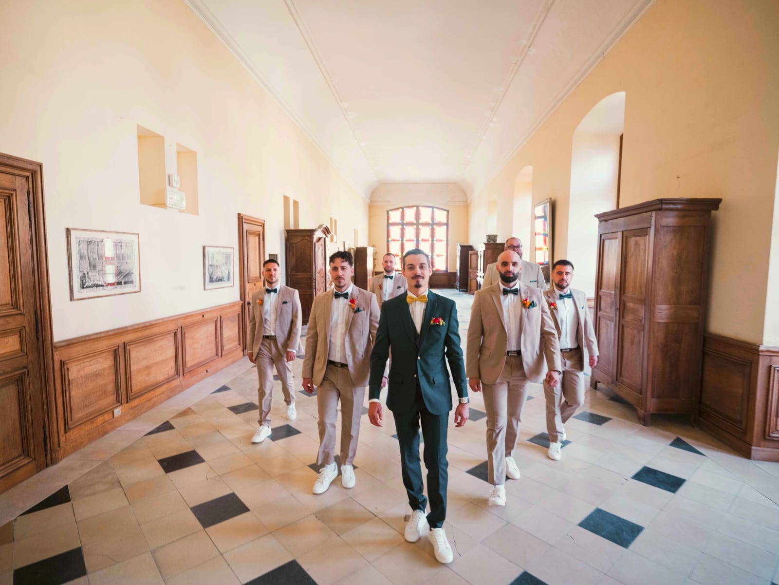 Le marié marche en tête de ses garçons d'honneur dans un long couloir au carrelage noir et blanc et aux boiseries, mariage à l'Abbaye de Longpont, par Jean-Baptiste Argyre (Jaysphotography)