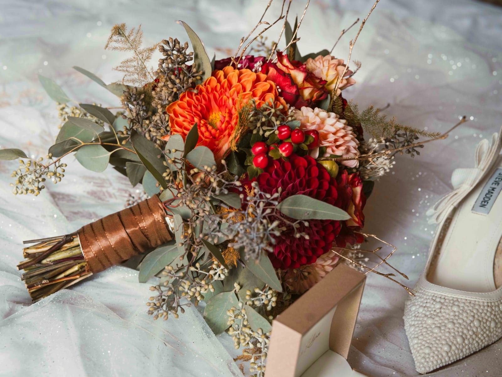 Bouquet de dahlias rouges, orange et pêche, baies d'hypericum et eucalyptus, tiges entourées de satin cuivré, à côté d'escarpins Steve Madden brodés de perles, mariage à l'Abbaye de Longpont, par Jean-Baptiste Argyre (Jaysphotography)