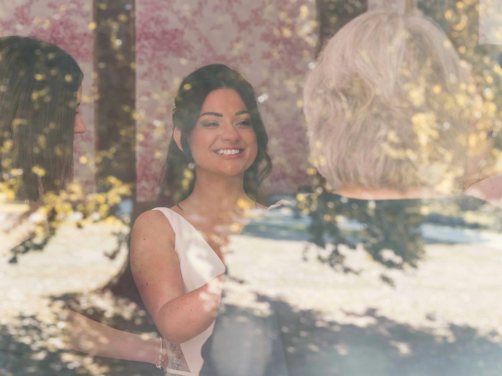 La mariée souriante photographiée à travers une vitre où se reflètent les arbres du parc, mariage à l'Abbaye de Longpont, par Jean-Baptiste Argyre (Jaysphotography)