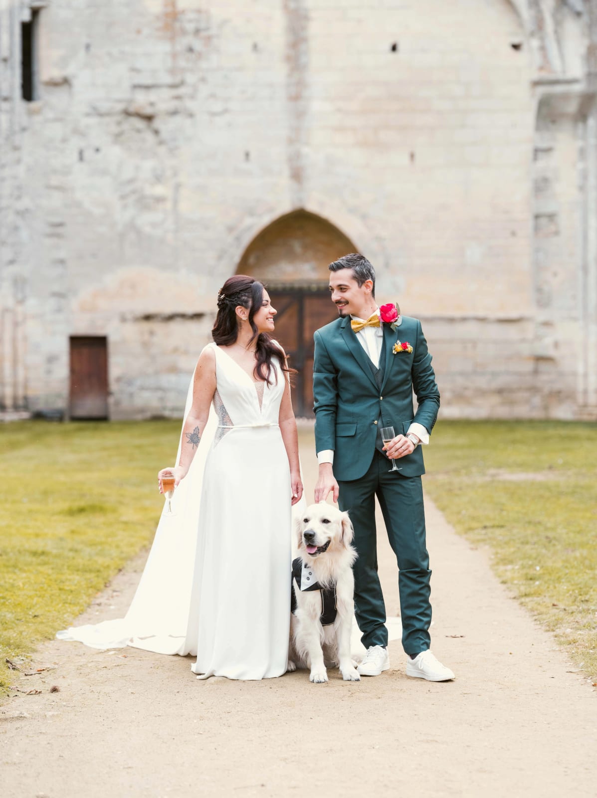 Les mariés dans l'allée des ruines de l'abbatiale avec un golden retriever en plastron de smoking, coupe de champagne à la main, mariage à l'Abbaye de Longpont, par Jean-Baptiste Argyre (Jaysphotography)