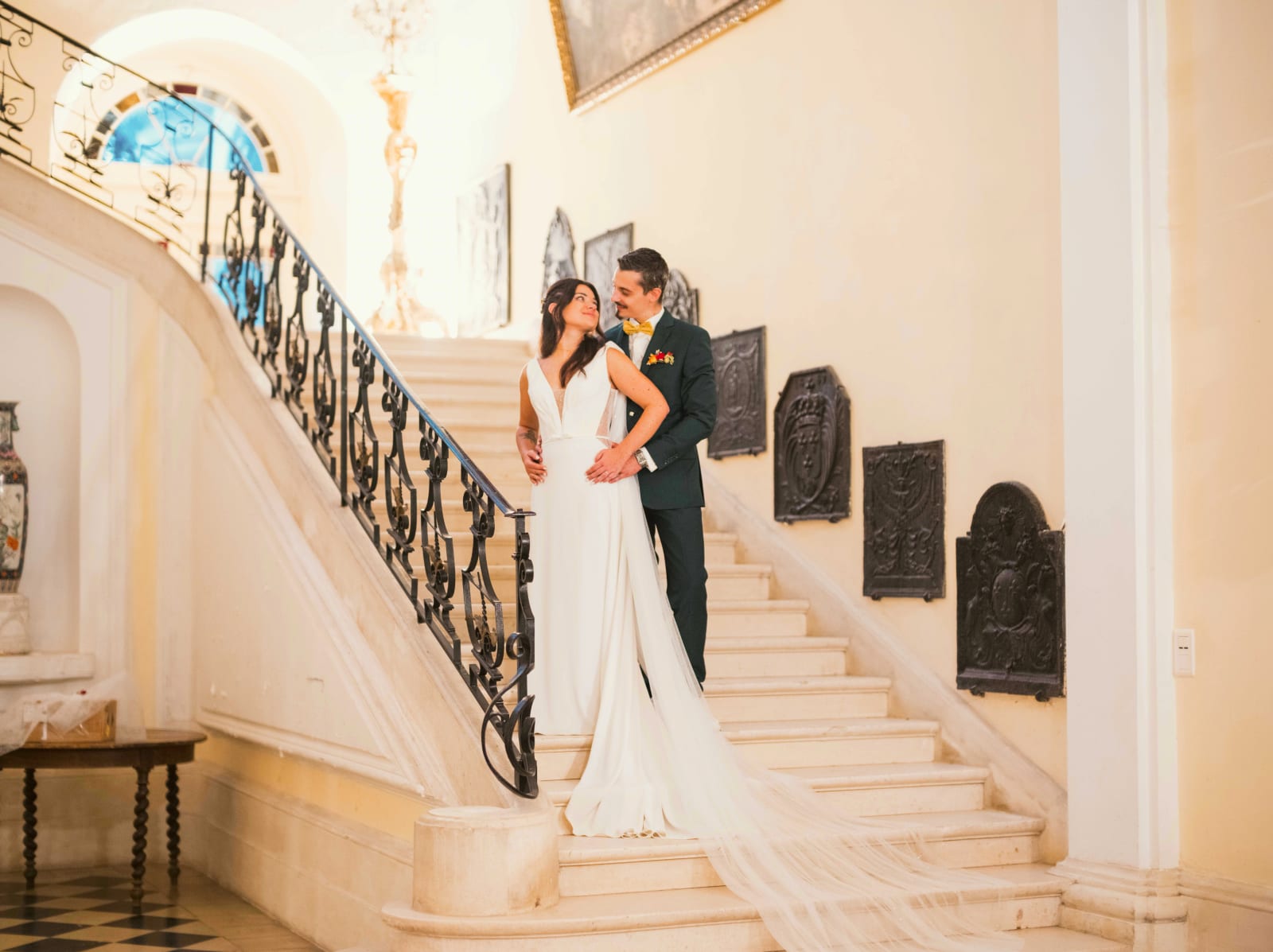 Les mariés enlacés sur le grand escalier de pierre à rampe en fer forgé, plaques de cheminée en fonte au mur, mariage à l'Abbaye de Longpont, par Jean-Baptiste Argyre (Jaysphotography)
