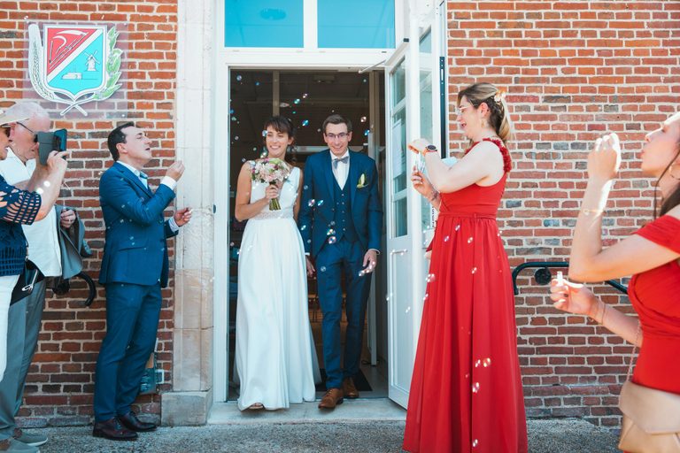 Sortie de la mairie de Catenoy sous les bulles de savon après le mariage civil et le baptême de Léo, façade de brique rouge et invités applaudissant
