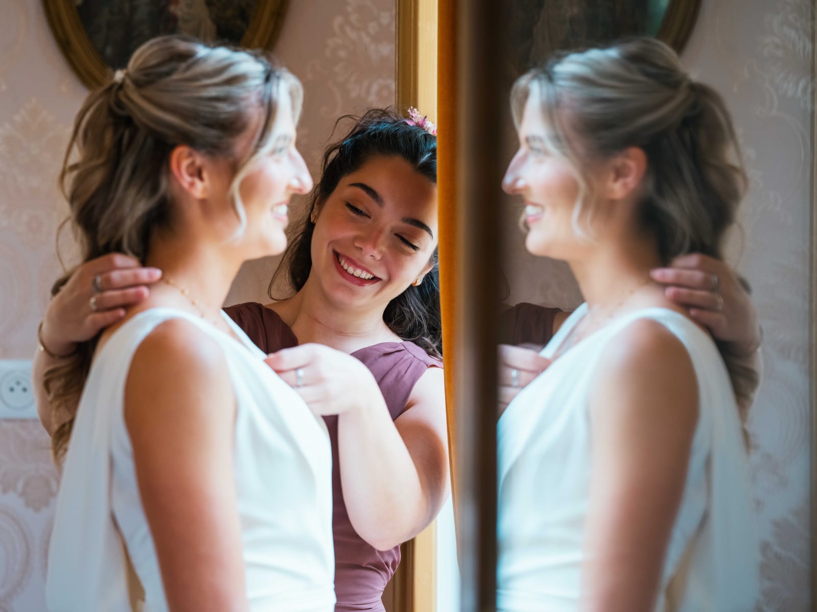 Mathilde en robe blanche échange un sourire complice avec sa demoiselle d'honneur en parme devant un miroir doré, mariage au Château de Moliens, par Jean-Baptiste Argyre (Jaysphotography)