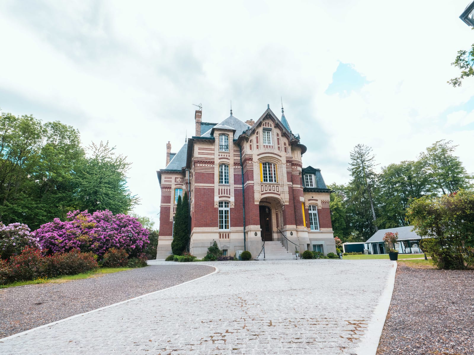 La façade en briques du Château de Moliens et ses rhododendrons en fleurs au printemps, mariage au Château de Moliens, par Jean-Baptiste Argyre (Jaysphotography)