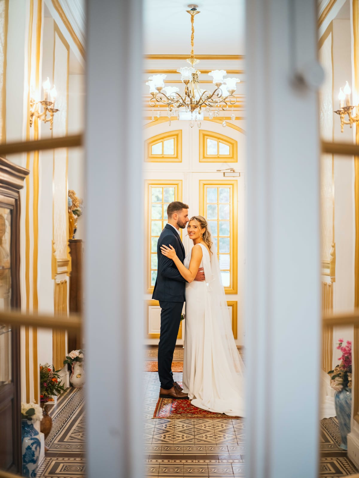 Mathilde et Paul enlacés dans un salon doré du Château de Moliens, cadrés à travers la double porte entrouverte, mariage au Château de Moliens, par Jean-Baptiste Argyre (Jaysphotography)