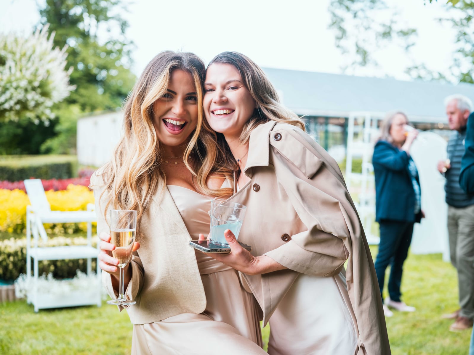 Deux invitées souriantes trinquent au champagne dans le parc du Château de Moliens pendant le vin d'honneur, mariage au Château de Moliens, par Jean-Baptiste Argyre (Jaysphotography)