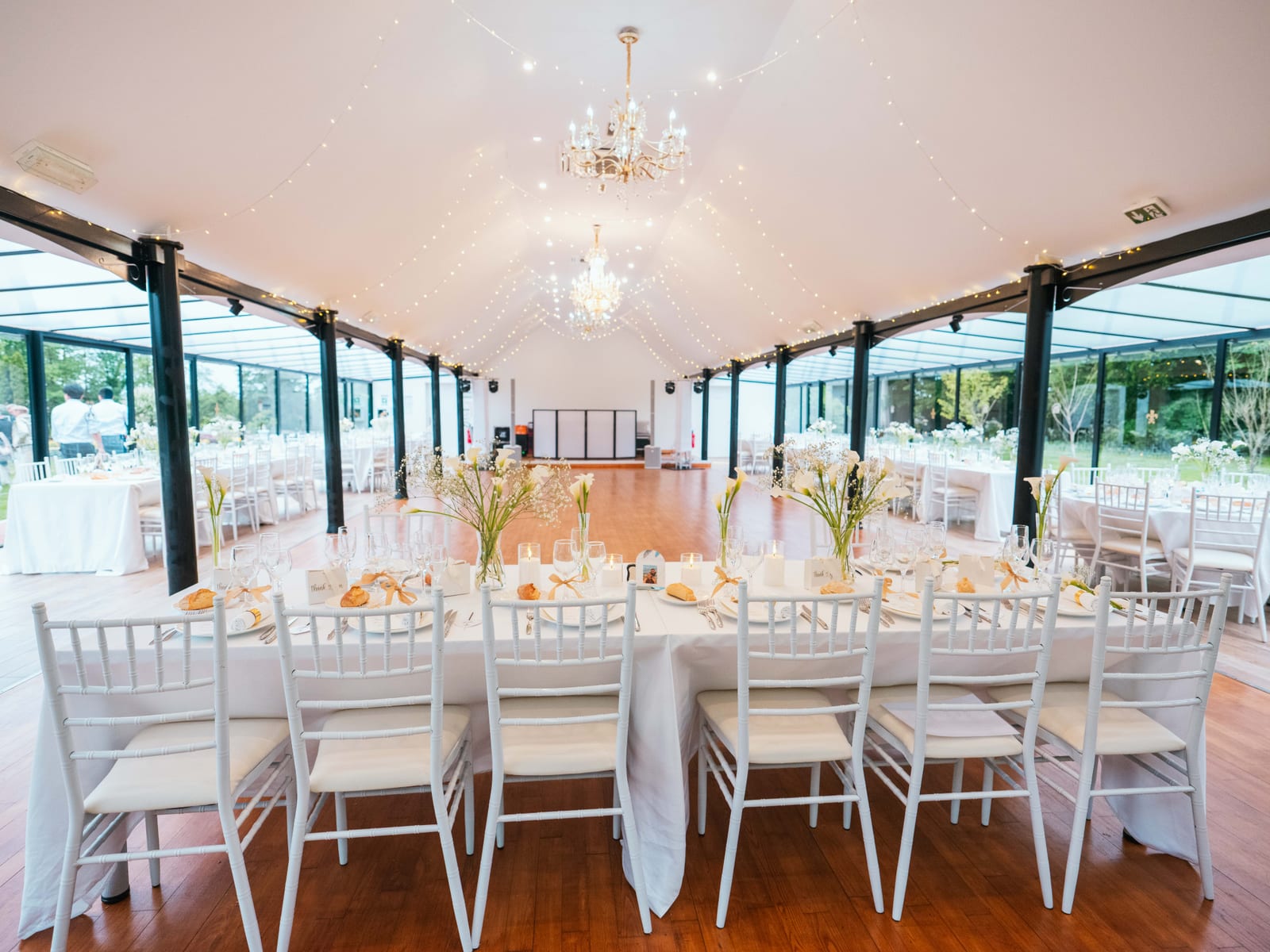 La salle de réception vitrée du Château de Moliens dressée en blanc, lustre en cristal et guirlandes au plafond, mariage au Château de Moliens, par Jean-Baptiste Argyre (Jaysphotography)