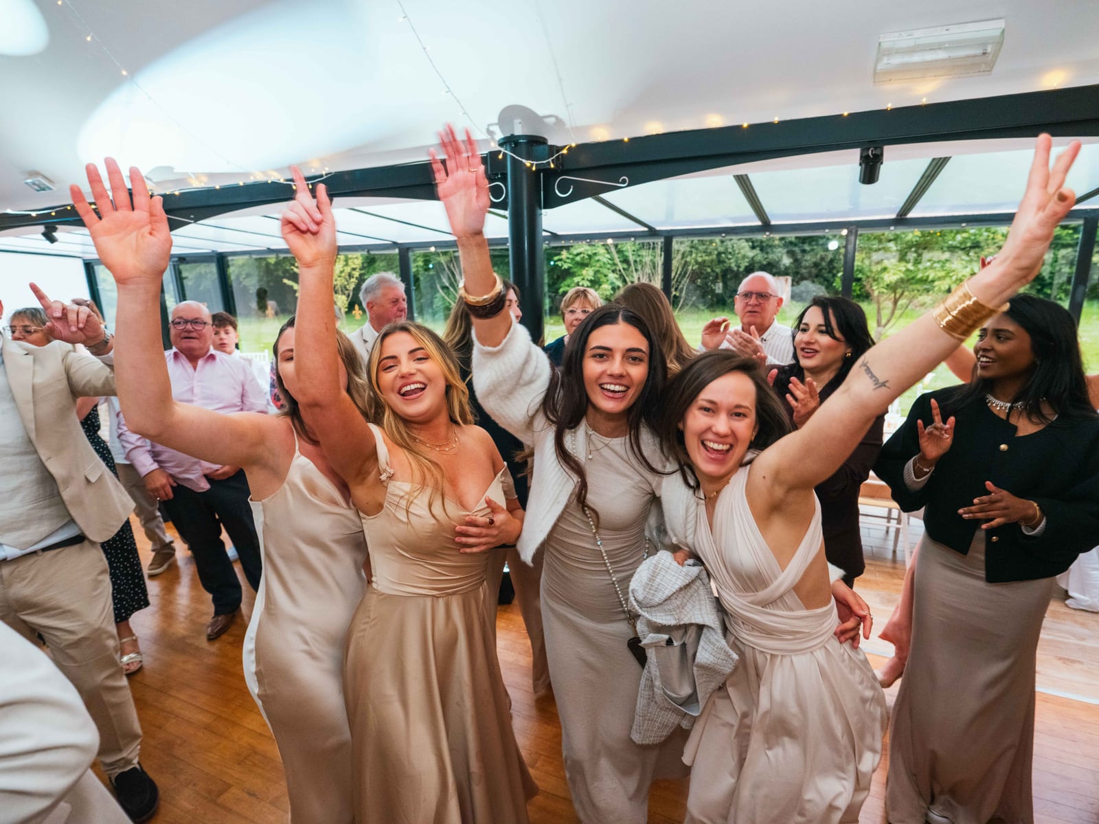 Invitées en robes dorées, bras levés sur la piste de danse pendant la soirée du mariage de Mathilde et Paul, mariage au Château de Moliens, par Jean-Baptiste Argyre (Jaysphotography)