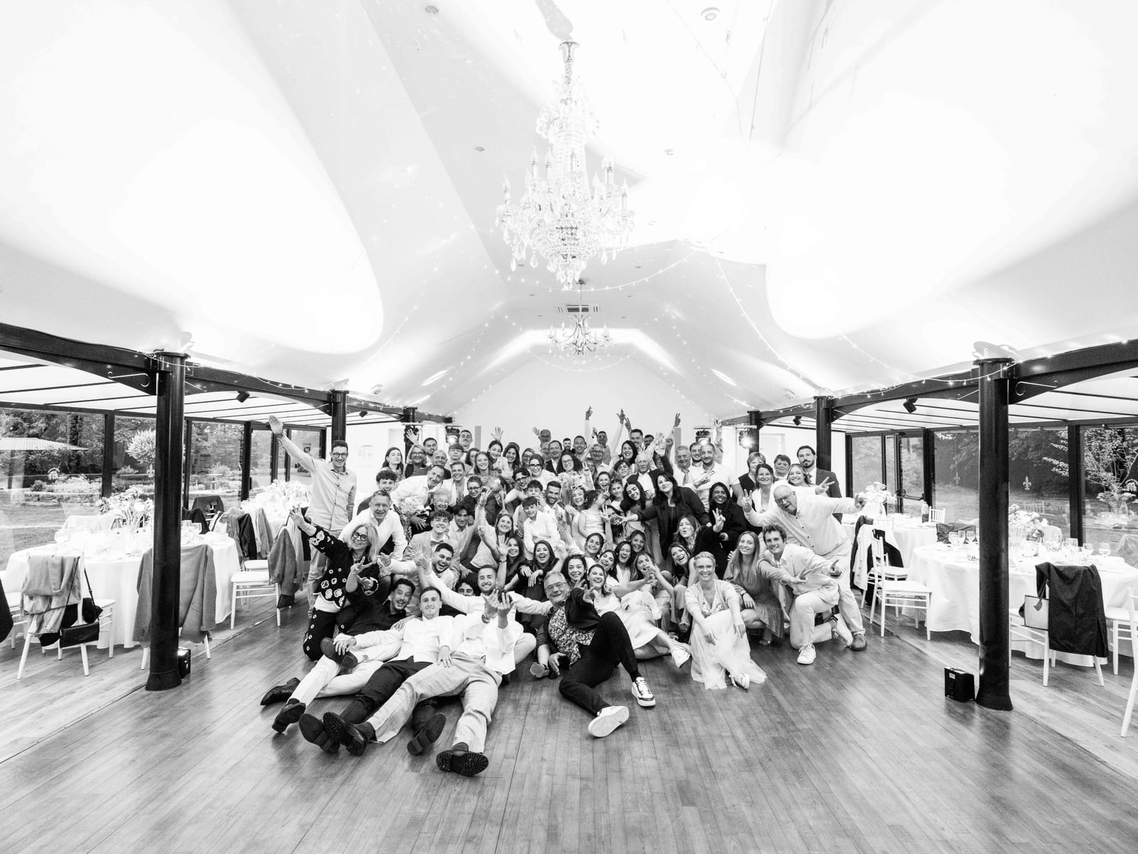 Photo de groupe de tous les invités du mariage réunis sur la piste sous le lustre, en noir et blanc, mariage au Château de Moliens, par Jean-Baptiste Argyre (Jaysphotography)