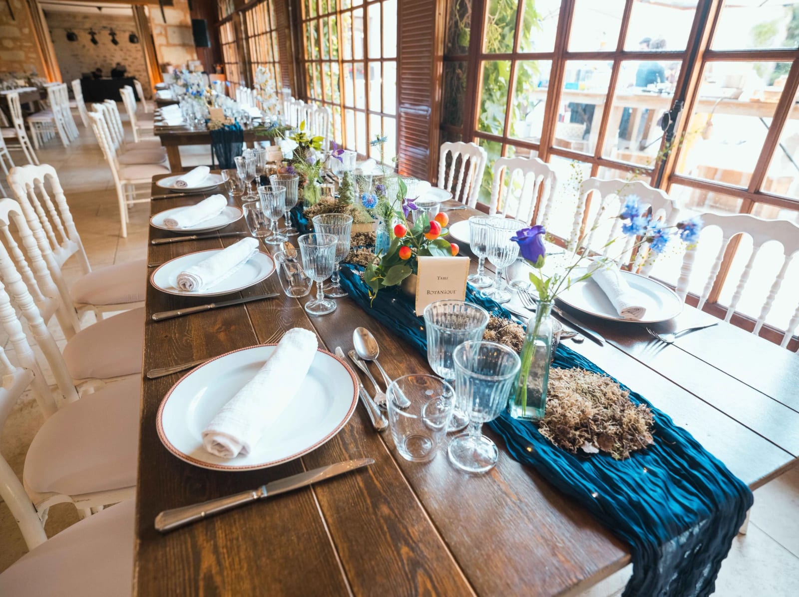 Longue table en bois brut au Château de Pontarmé, chemin de table en voile bleu paon, verres à facettes et compositions de fleurs des champs, mariage au Château de Pontarmé, par Jean-Baptiste Argyre (Jaysphotography)