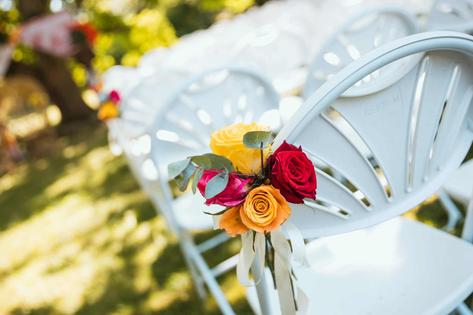 Chaises de la cérémonie laïque fleuries de roses rouges et jaunes, mariage au La Ferme de la Biza, par Jean-Baptiste Argyre (Jaysphotography)