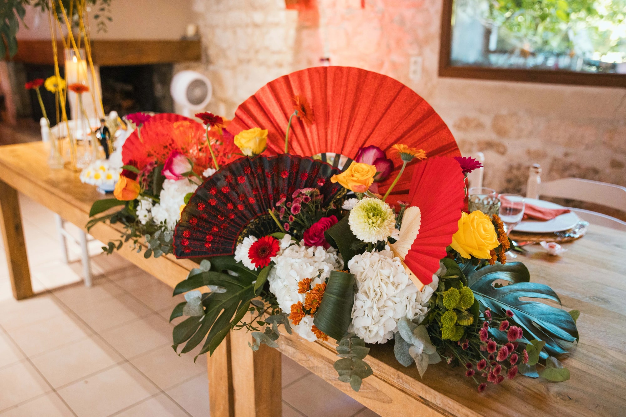 Composition exotique de la table d'honneur, éventail rouge et fleurs vives, mariage au La Ferme de la Biza, par Jean-Baptiste Argyre (Jaysphotography)