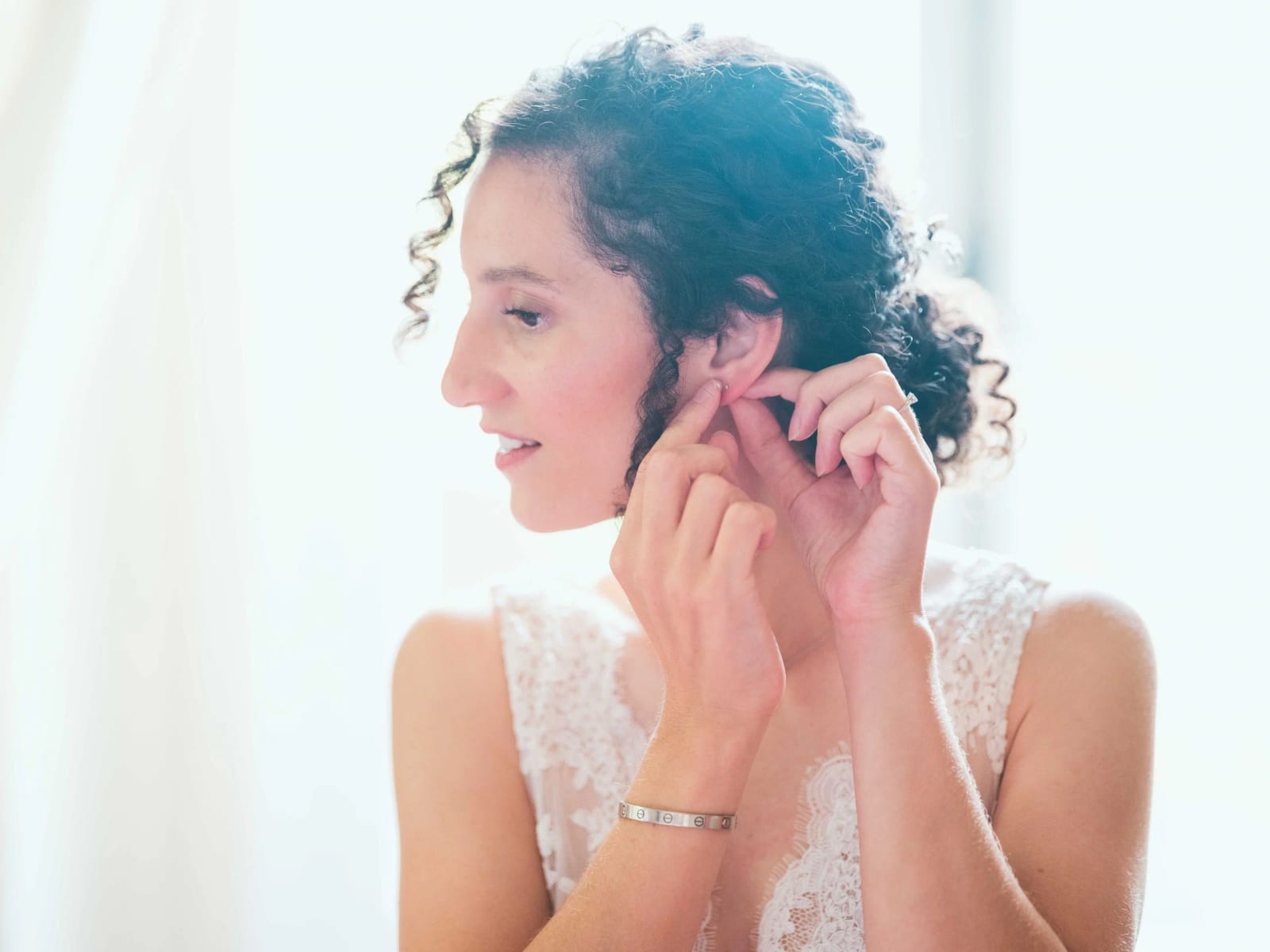 La mariée accroche ses boucles d'oreilles à contre-jour devant la fenêtre, mariage au Château de Reilly, par Jean-Baptiste Argyre (Jaysphotography)