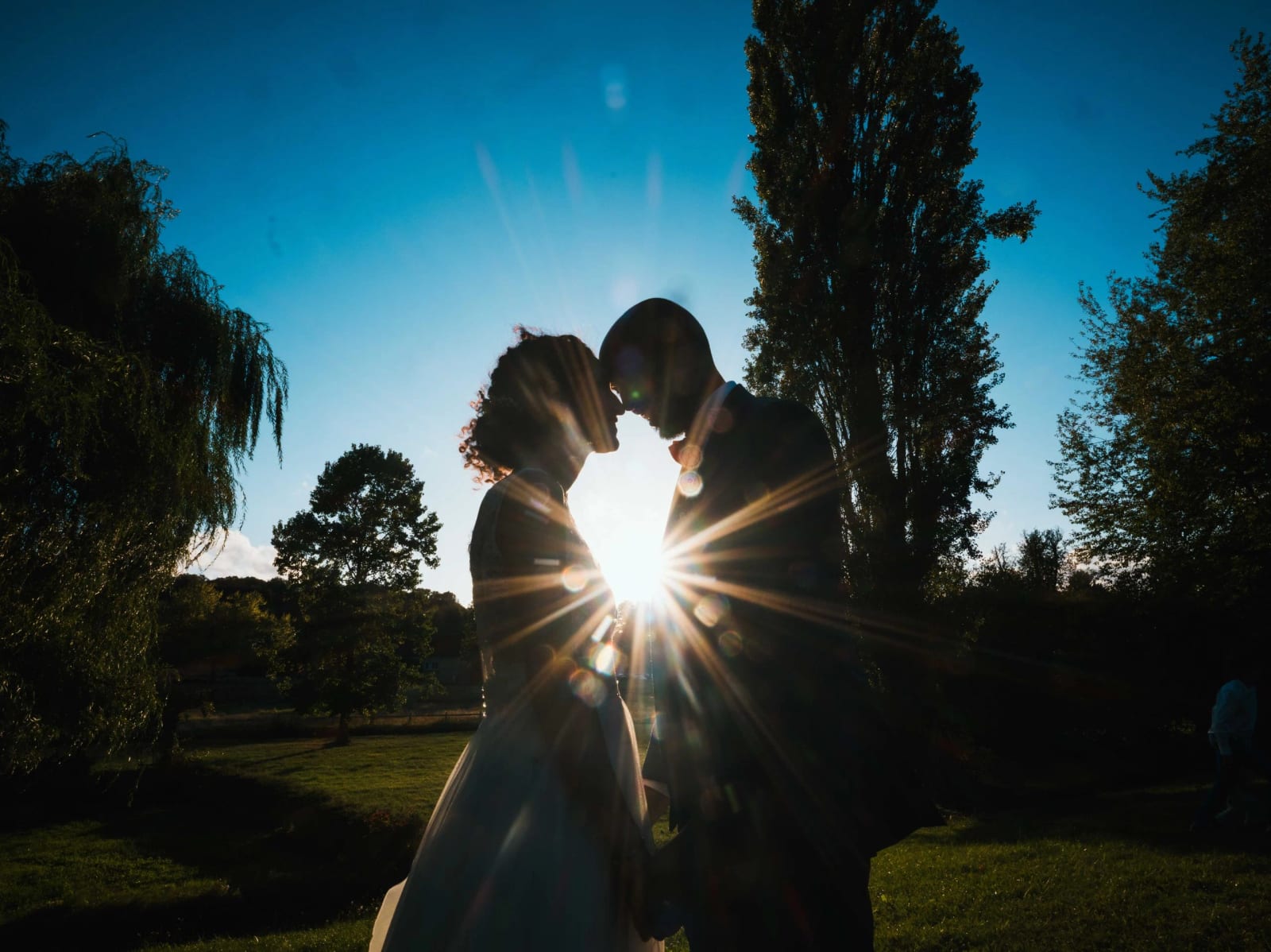 Silhouettes des mariés à contre-jour dans le parc, l'étoile du soleil entre leurs visages, mariage au Château de Reilly, par Jean-Baptiste Argyre (Jaysphotography)
