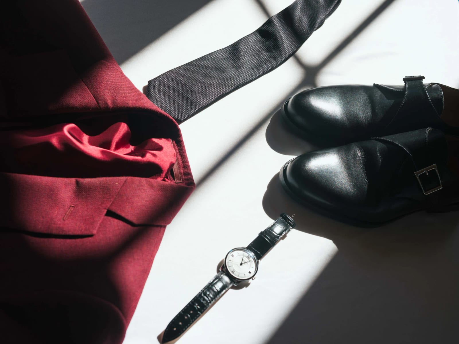 Souliers noirs, nœud papillon, montre à bracelet de cuir et veste lie-de-vin du marié posés dans une lame de soleil, préparatifs au Château de Moliens, mariage au Château de Moliens, par Jean-Baptiste Argyre (Jaysphotography)