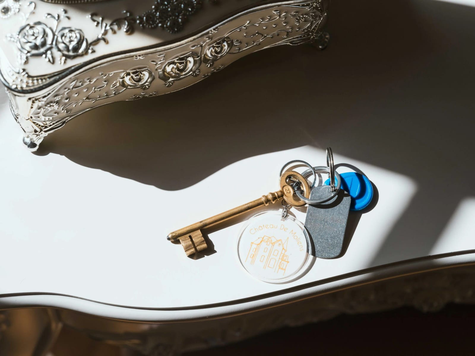 Clé ancienne à anneau ouvragé et porte-clés du Château de Moliens posés sur un plateau d'argent, mariage au Château de Moliens, par Jean-Baptiste Argyre (Jaysphotography)
