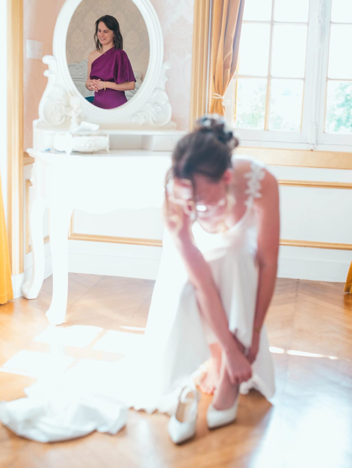 La mariée enfile ses chaussures sous un portrait ancien, lumière de fenêtre, préparatifs au Château de Moliens, mariage au Château de Moliens, par Jean-Baptiste Argyre (Jaysphotography)