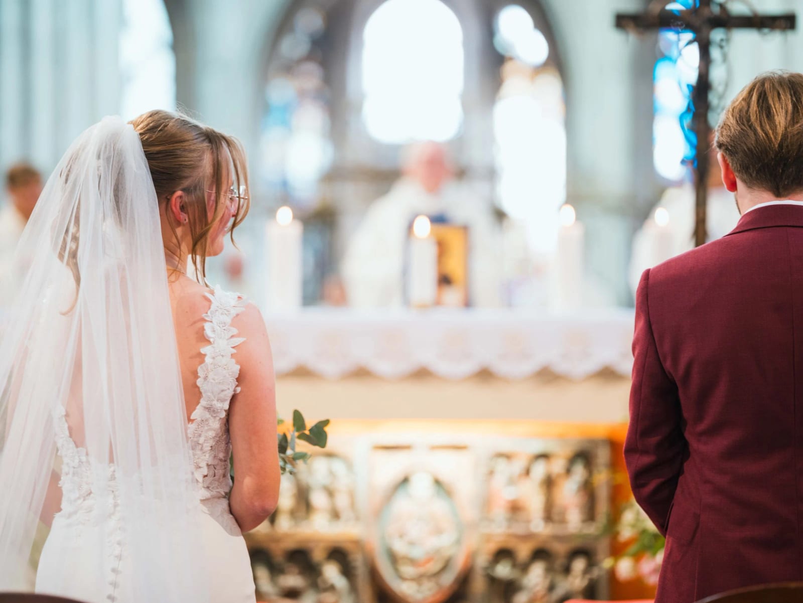 Les mariés de dos devant l'autel de l'église Saint-Étienne de Beauvais pendant la messe de mariage, verrière bleue au fond, mariage au Château de Moliens, par Jean-Baptiste Argyre (Jaysphotography)
