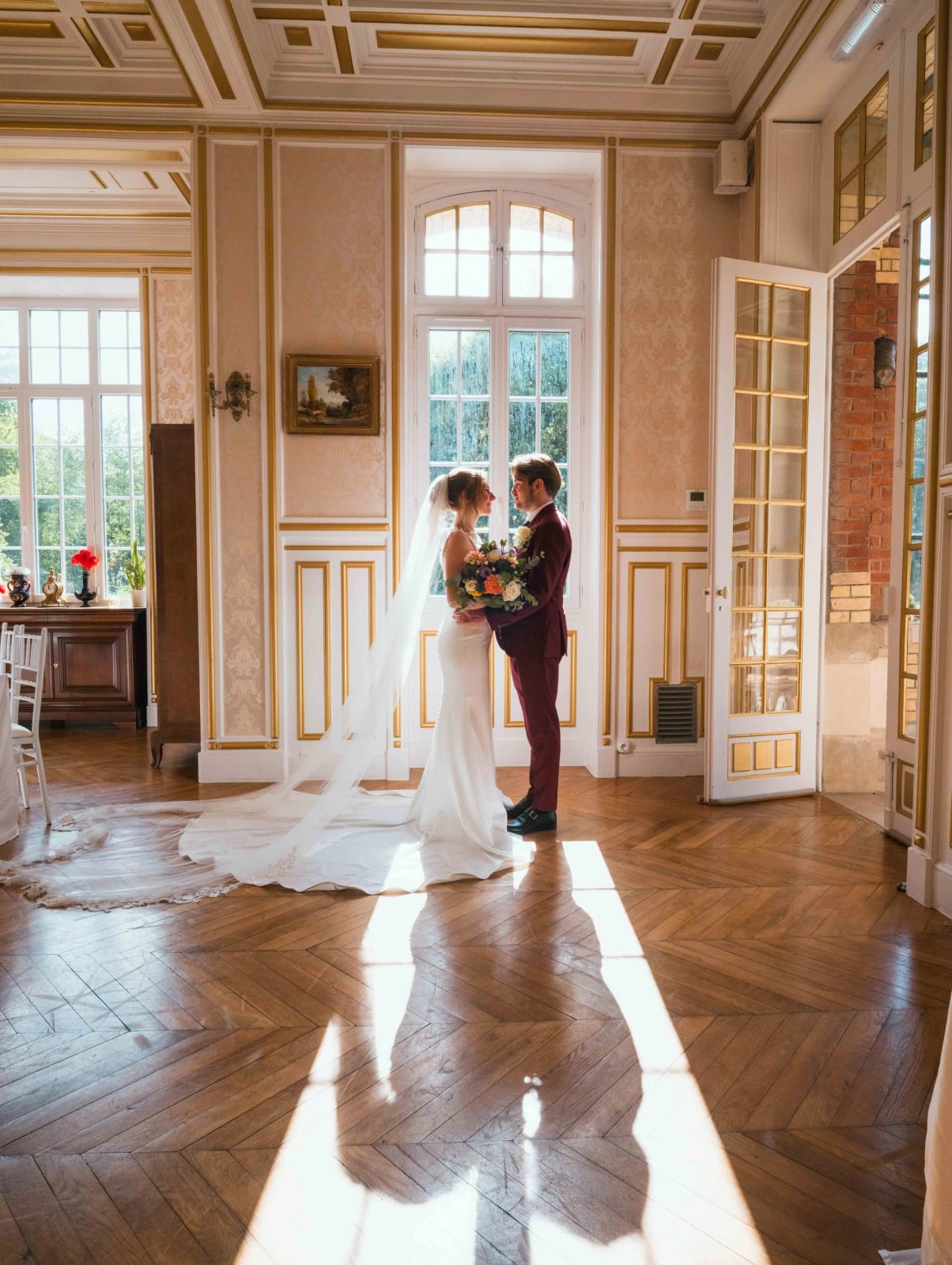 Les mariés enlacés dans un salon du Château de Moliens, traîne déployée sur le parquet, lumière rasante des hautes fenêtres, mariage au Château de Moliens, par Jean-Baptiste Argyre (Jaysphotography)