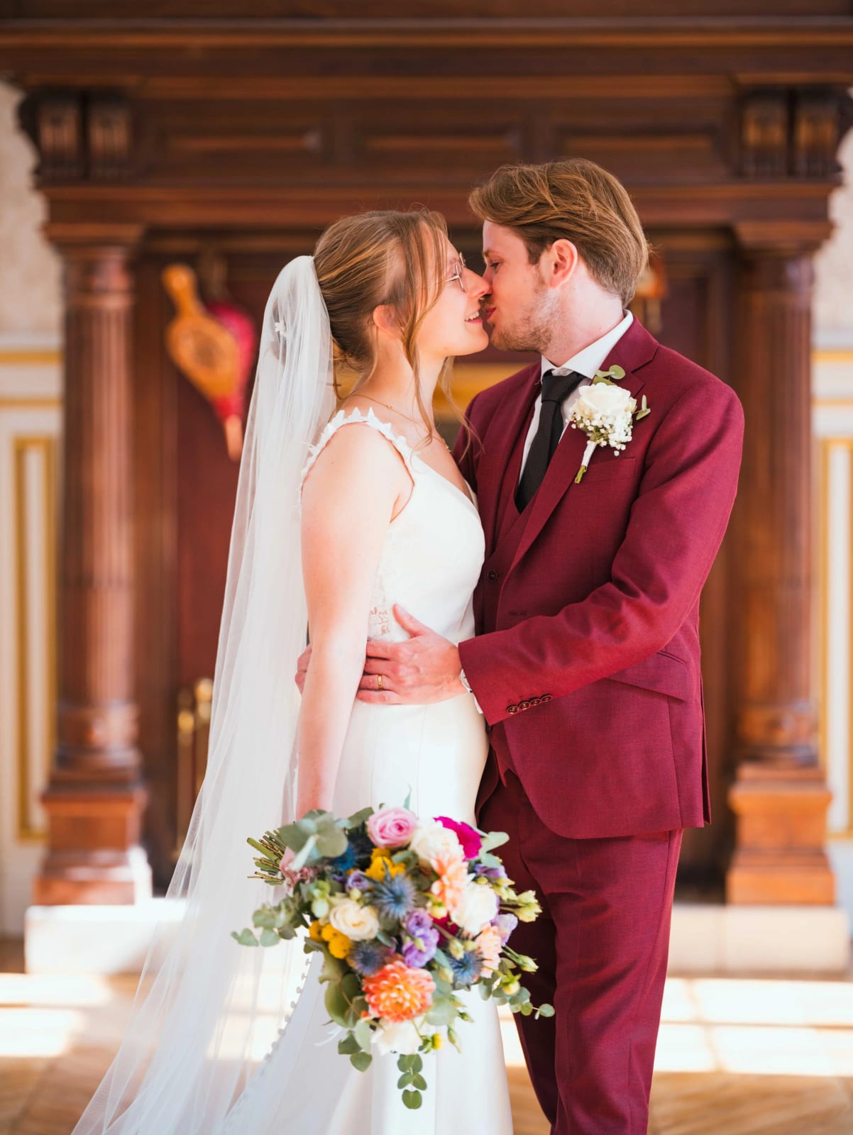 Les mariés s'embrassent devant la boiserie sculptée du hall du Château de Moliens, la mariée tient son bouquet, mariage au Château de Moliens, par Jean-Baptiste Argyre (Jaysphotography)