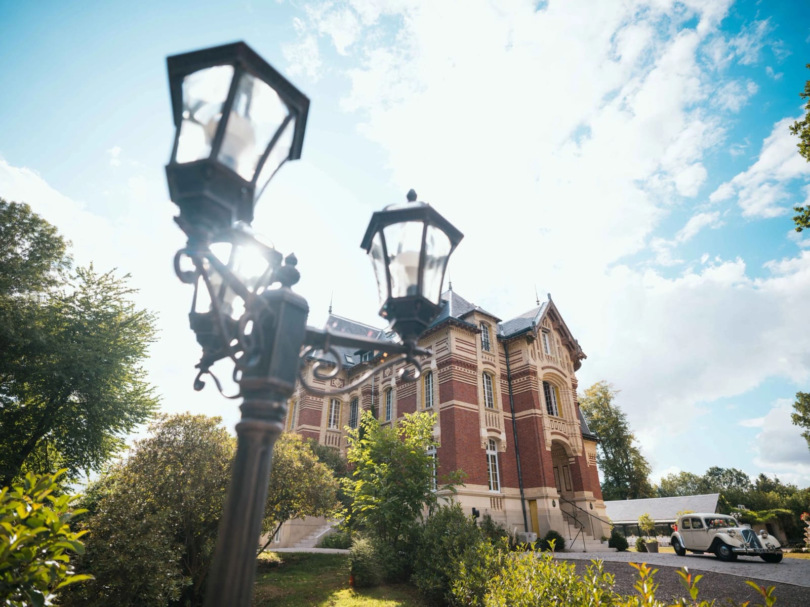 La façade du Château de Moliens sous un ciel d'août, vieux lampadaire de la cour au premier plan, mariage au Château de Moliens, par Jean-Baptiste Argyre (Jaysphotography)