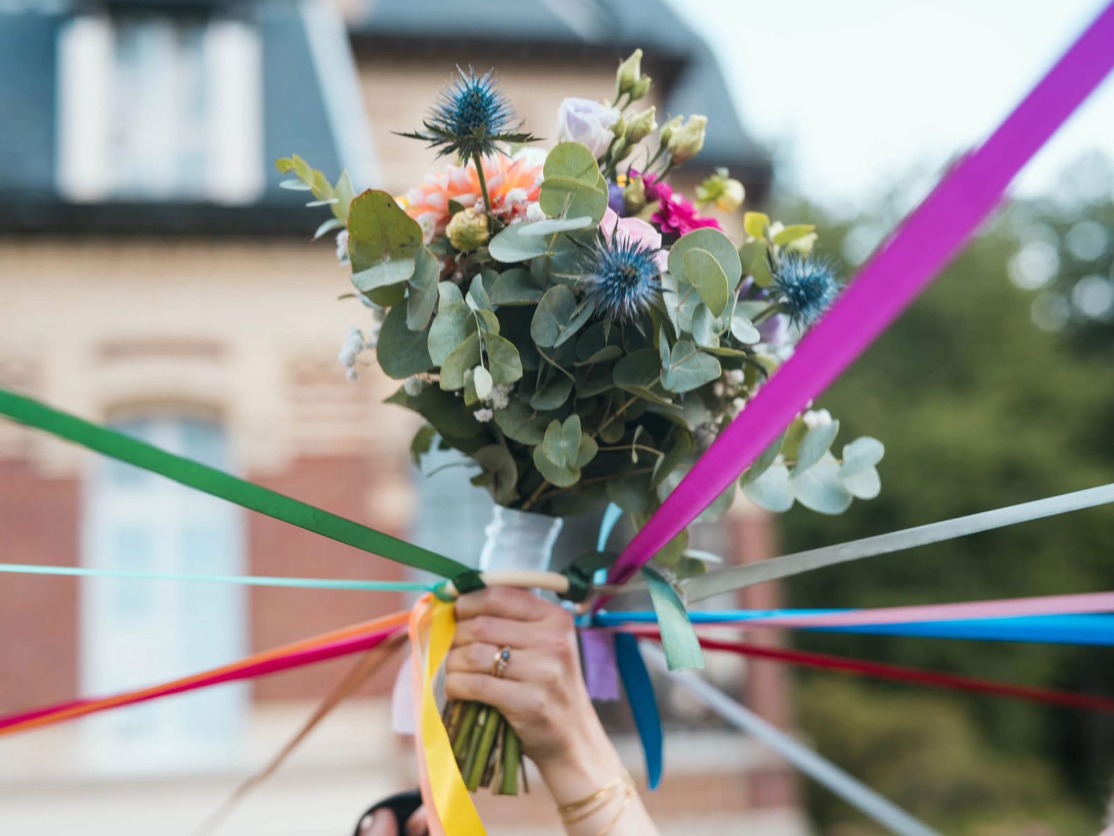 Le bouquet de la mariée au centre des rubans multicolores : eucalyptus, chardons bleus et corolles orangées, Château de Moliens, mariage au Château de Moliens, par Jean-Baptiste Argyre (Jaysphotography)
