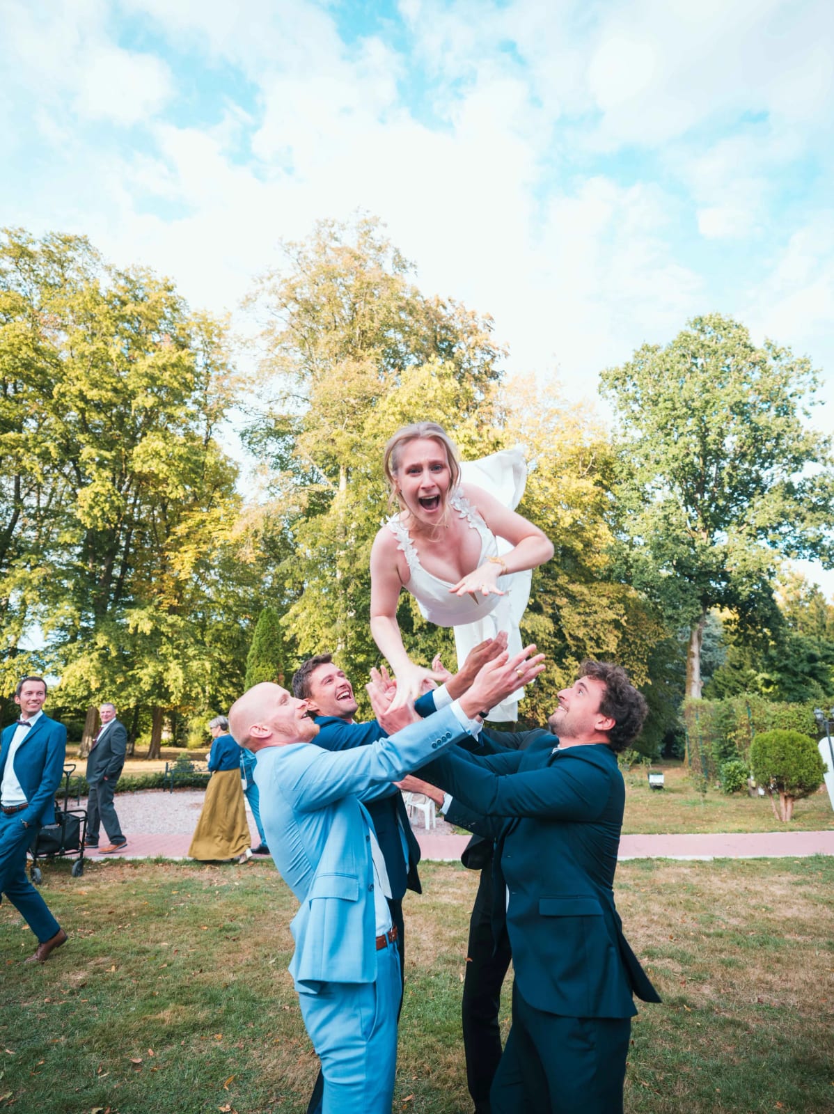 La mariée jetée en l'air par des amis en costume sous les arbres du parc du Château de Moliens, mariage au Château de Moliens, par Jean-Baptiste Argyre (Jaysphotography)
