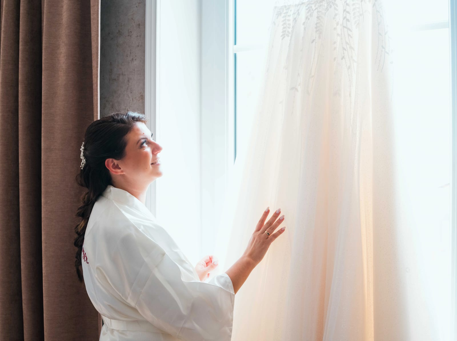 Pauline en peignoir découvrant sa robe suspendue à la fenêtre, mariage au Château des Granges, par Jean-Baptiste Argyre (Jaysphotography)