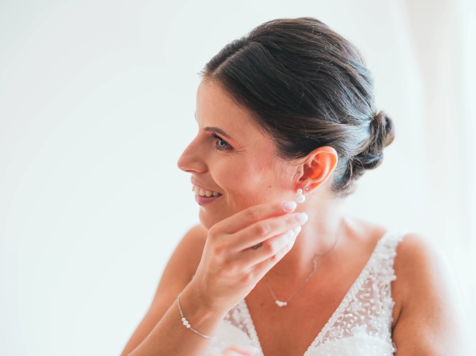 La mariée accroche ses boucles d'oreilles en perles, robe à décolleté en V brodée de perles, mariage au Château de Sainte-Claire, Berneuil-sur-Aisne, par Jean-Baptiste Argyre (Jaysphotography)