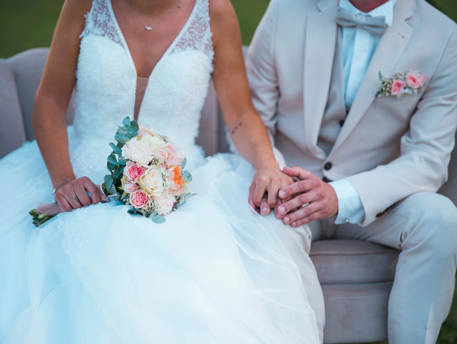 Les mariés assis sur une banquette de velours, main dans la main, bouquet de roses pêche et blanches, mariage au Château de Sainte-Claire, Berneuil-sur-Aisne, par Jean-Baptiste Argyre (Jaysphotography)