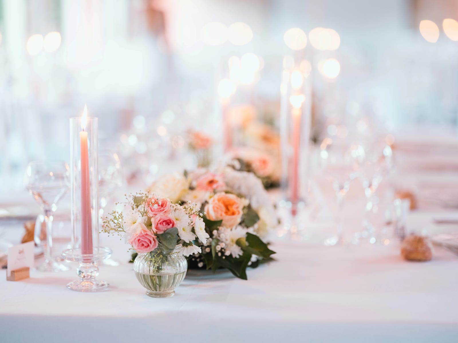 Table dressée : bougies roses, roses pêche dans un petit vase rond, verres et invitations sur nappe blanche, mariage au Château de Sainte-Claire, Berneuil-sur-Aisne, par Jean-Baptiste Argyre (Jaysphotography)