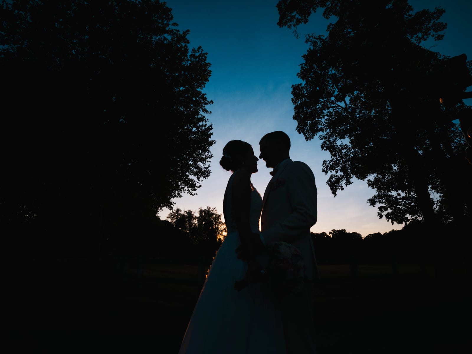 Silhouettes des mariés sous les arbres sur un ciel bleu profond, mariage au Château de Sainte-Claire, Berneuil-sur-Aisne, par Jean-Baptiste Argyre (Jaysphotography)