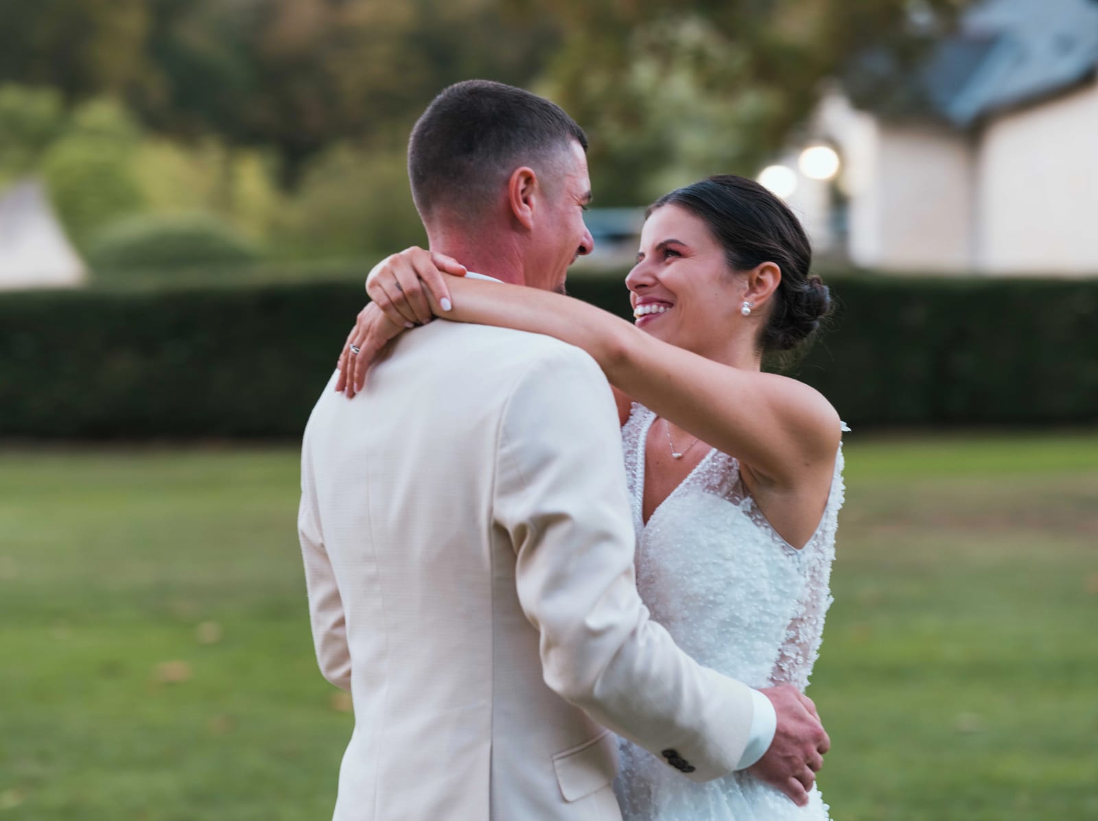 La mariée rit, les bras autour du cou du marié en costume beige, dans le parc, mariage au Château de Sainte-Claire, Berneuil-sur-Aisne, par Jean-Baptiste Argyre (Jaysphotography)