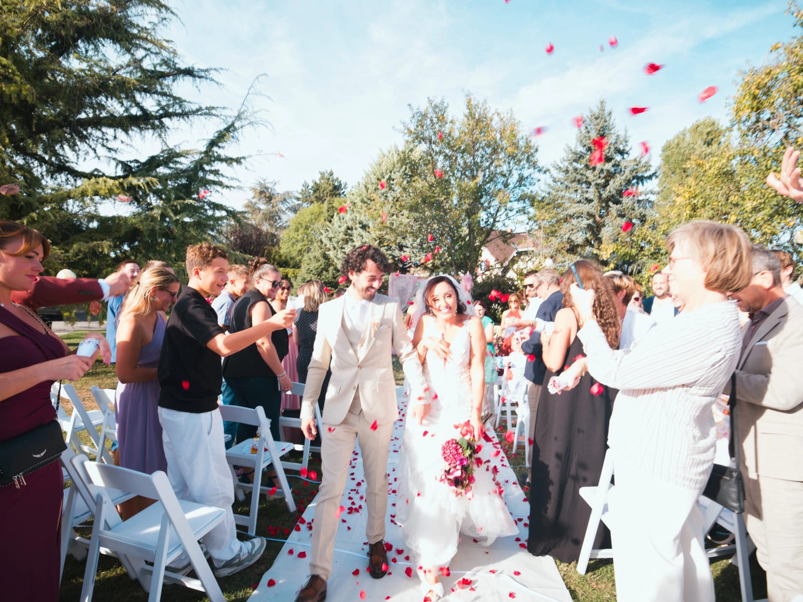 Sortie de cérémonie sur un tapis blanc sous une pluie de pétales rouges, invités de chaque côté de l'allée, mariage au Clos d'Amblaincourt, par Jean-Baptiste Argyre (Jaysphotography)