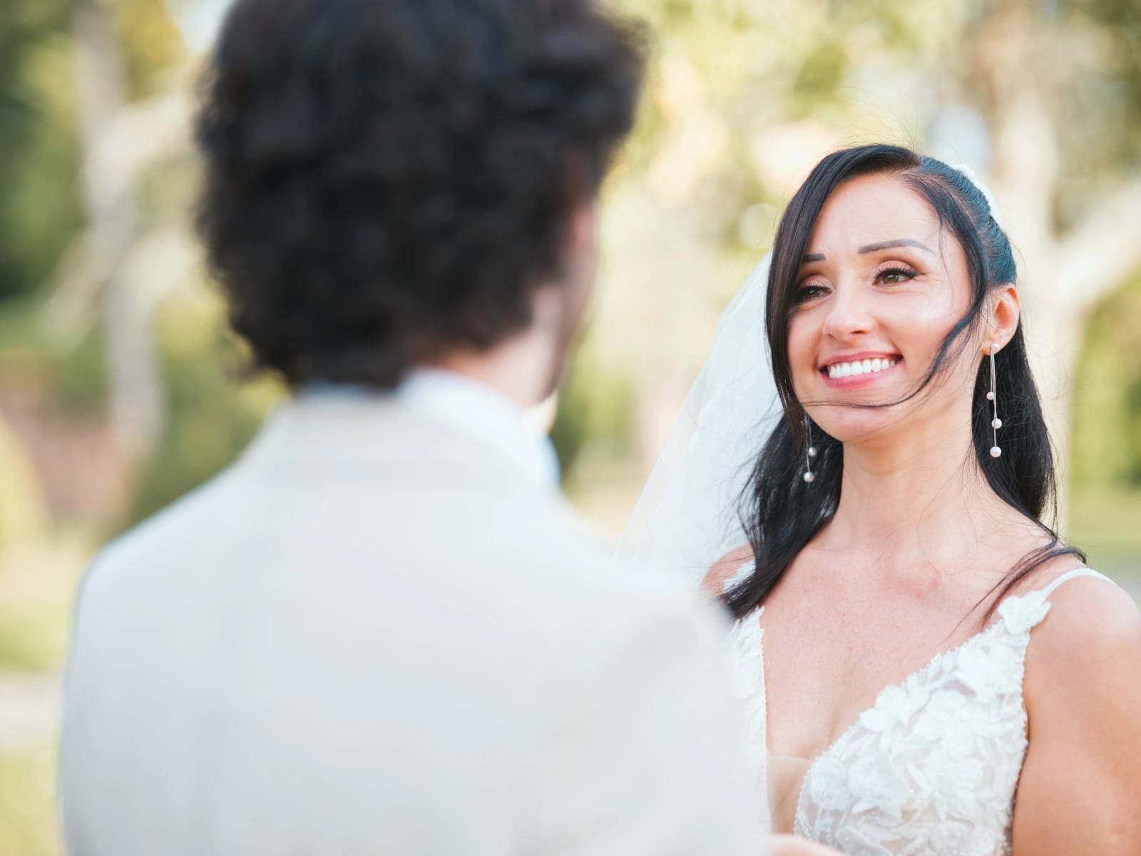 La mariée sourit au marié vu de dos, voile soulevé par le vent, mariage au Clos d'Amblaincourt, par Jean-Baptiste Argyre (Jaysphotography)
