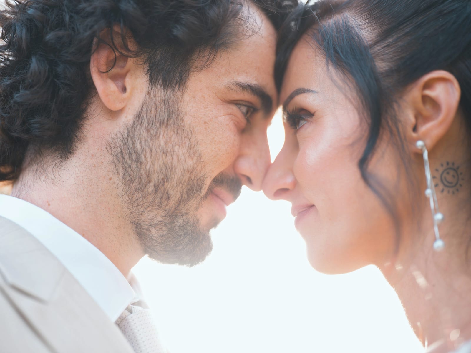 Gros plan des mariés nez contre nez, boucles d'oreilles en perles et petit soleil tatoué sous l'oreille de la mariée, mariage au Clos d'Amblaincourt, par Jean-Baptiste Argyre (Jaysphotography)