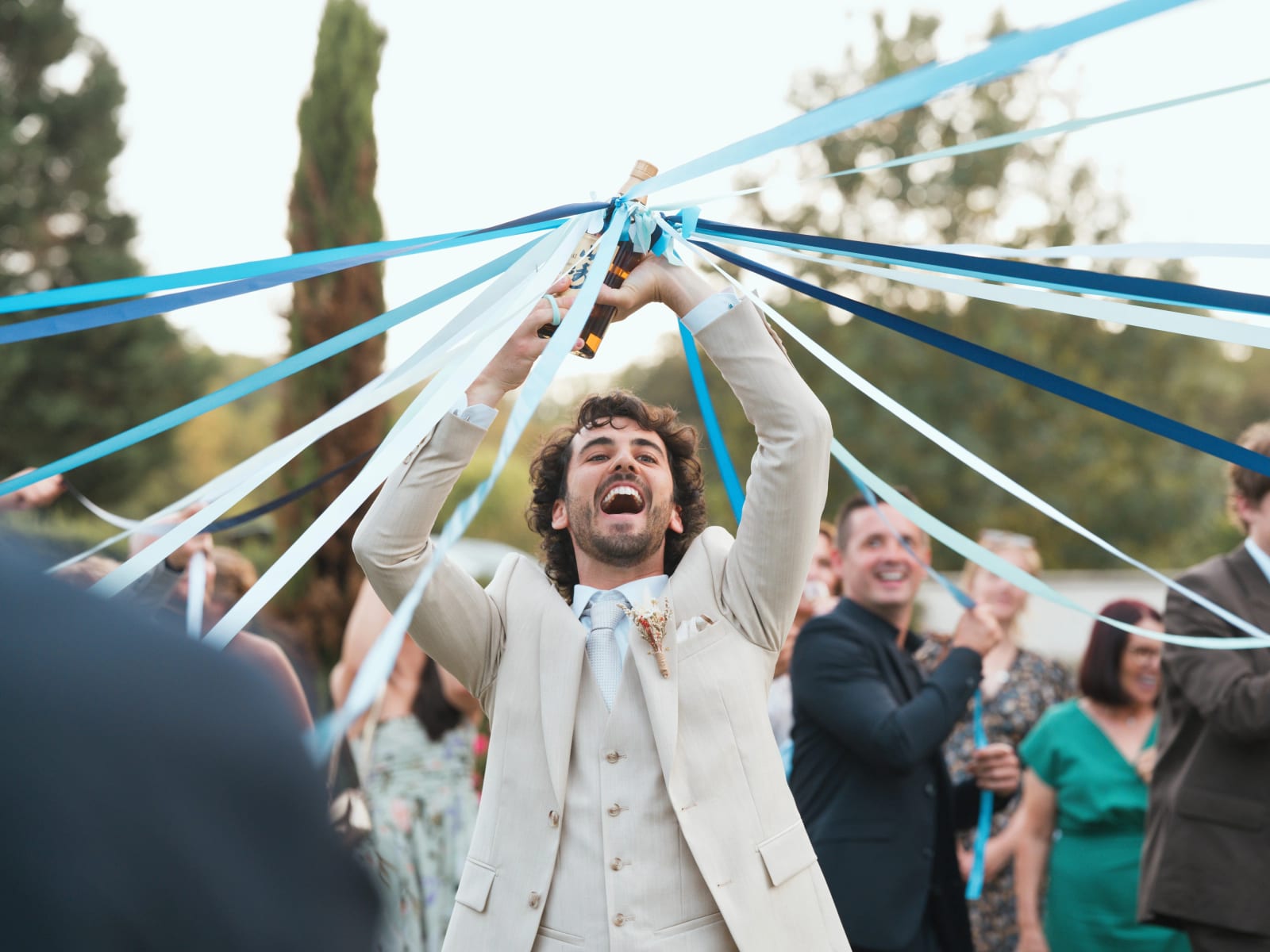 Ronde de la bouteille : le marié lève une bouteille reliée à des rubans bleus, éclat de rire, mariage au Clos d'Amblaincourt, par Jean-Baptiste Argyre (Jaysphotography)