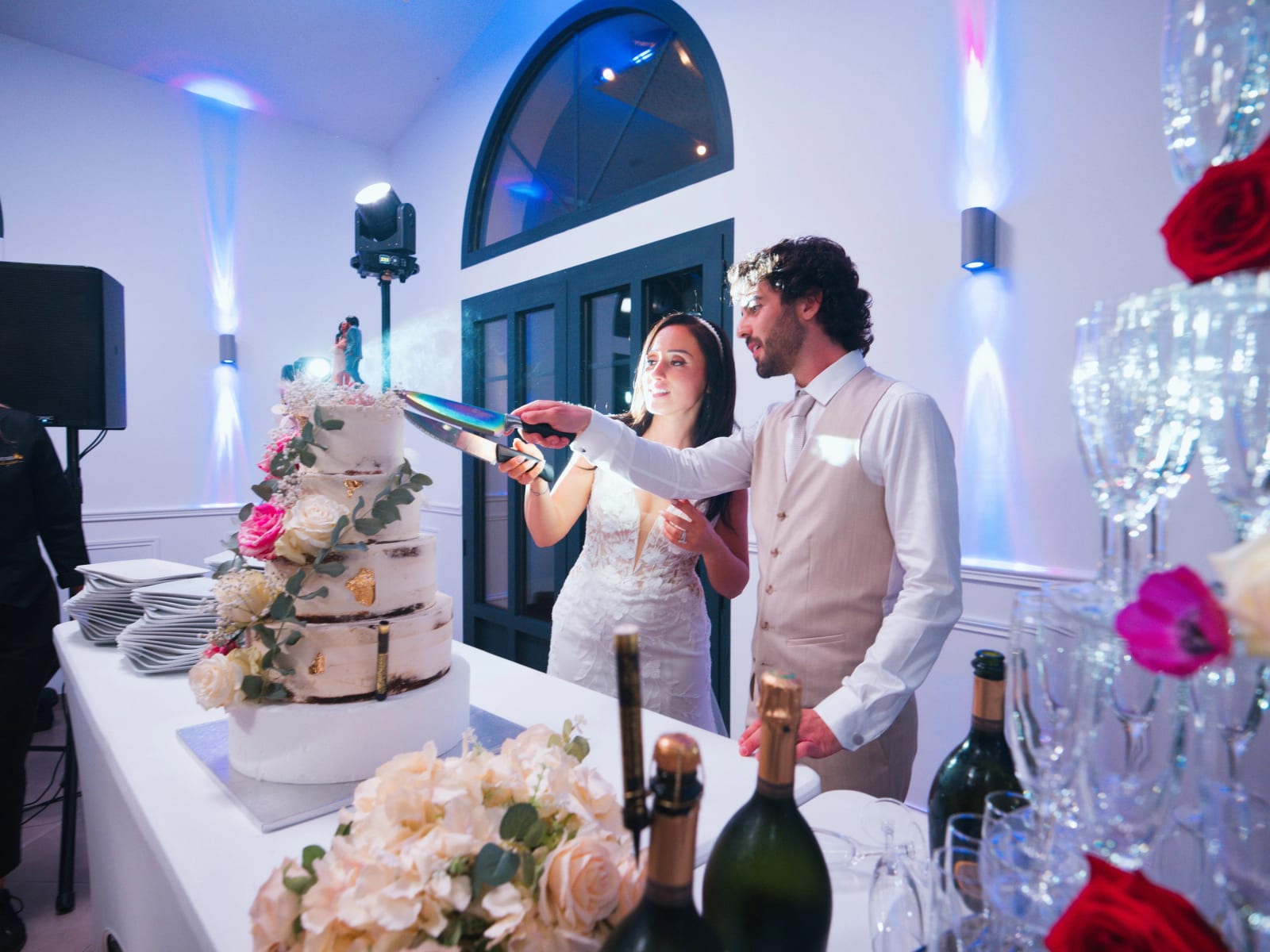 Les mariés coupent un naked cake de quatre étages à feuille d'or devant une porte-fenêtre en arc, pyramide de coupes de champagne, mariage au Clos d'Amblaincourt, par Jean-Baptiste Argyre (Jaysphotography)