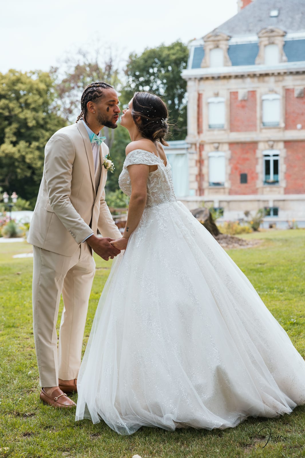 Marie et Benjamin en couleur sur la pelouse, facade rose du château en arrière-plan, costume beige et robe blanche, mariage au Château de Broyes, par Jean-Baptiste Argyre (Jaysphotography)