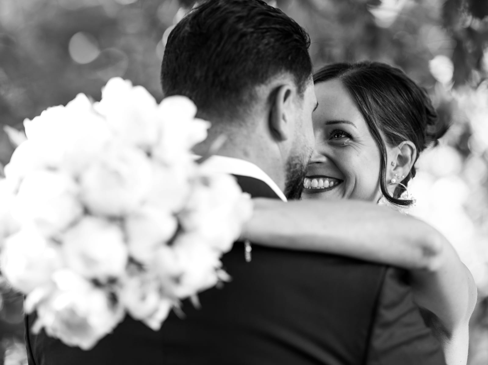 Portrait NB du couple enlacé, bouquet de fleurs blanches en gros plan, lumière douce et intimité après la mairie, mariage au Refuges des 3 Ours, par Jean-Baptiste Argyre (Jaysphotography)