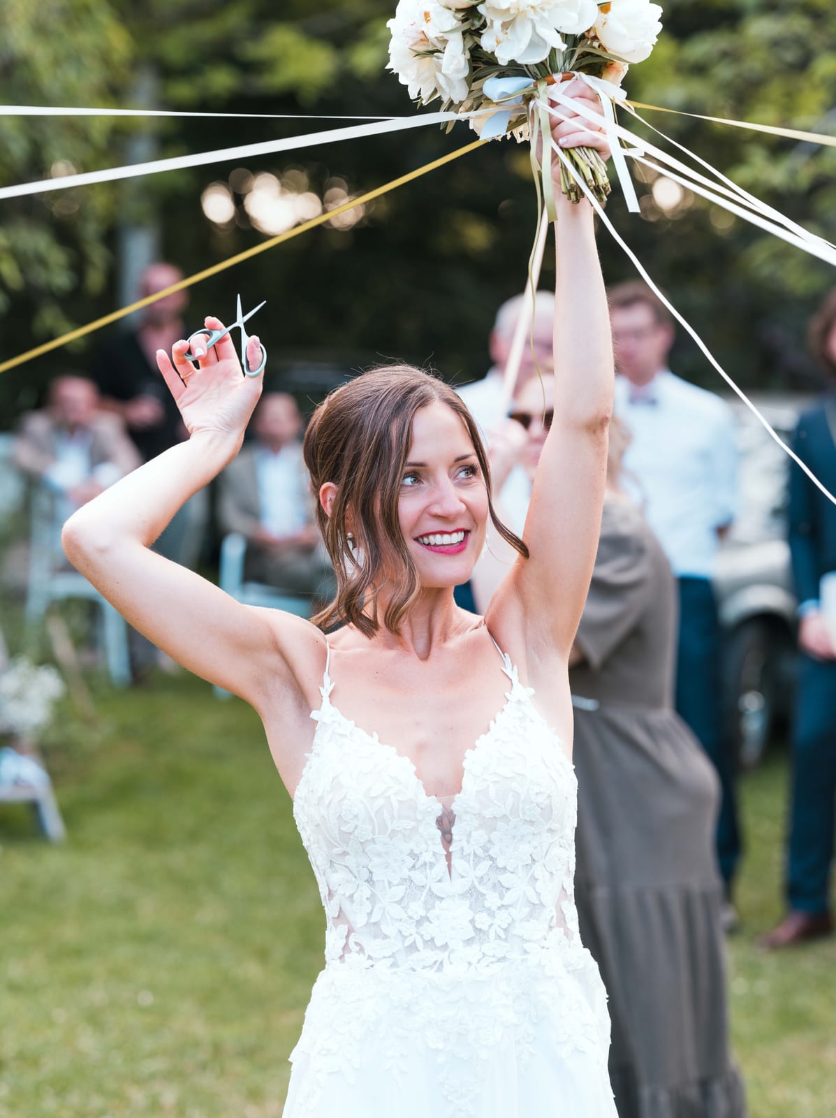 Mathilde bras levés, ruban coloré à la main, au centre du jeu du ruban avec les invités réunis autour d'elle, mariage au Refuges des 3 Ours, par Jean-Baptiste Argyre (Jaysphotography)