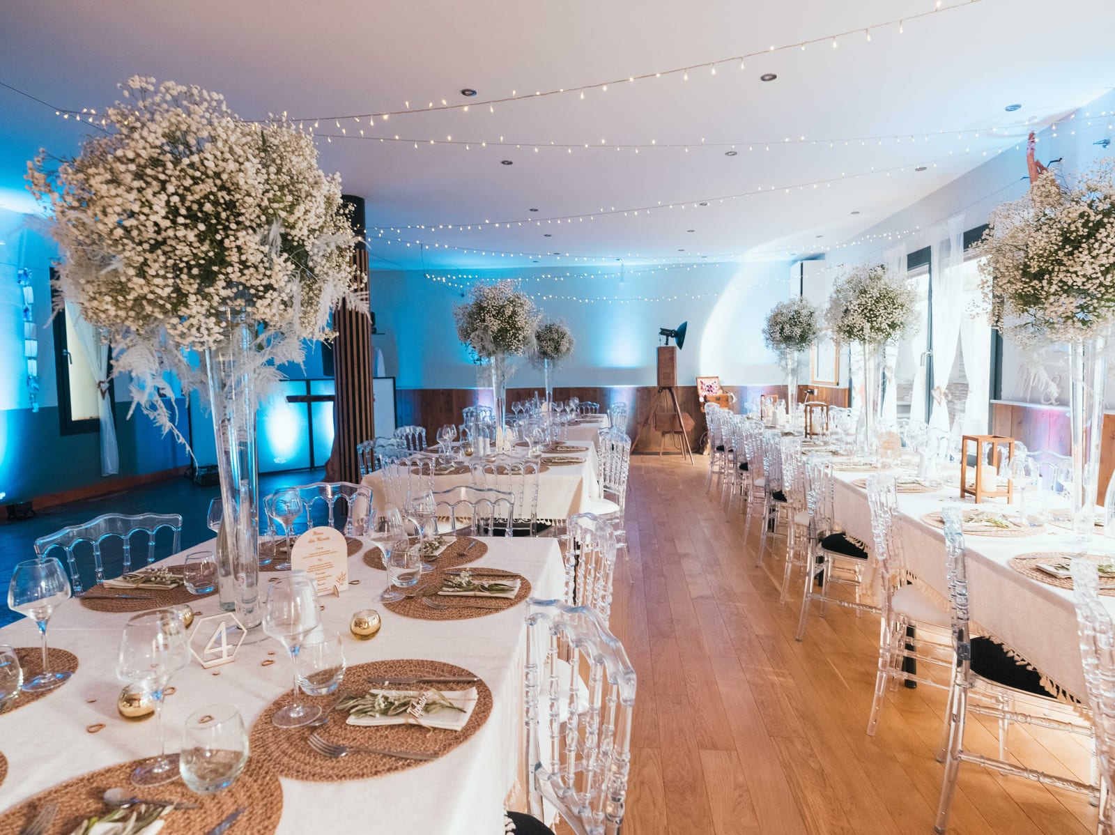 Salle de réception des Refuges des 3 Ours dressée pour le dîner, tables rondes avec compositions florales hautes en gypsophile et guirlandes lumineuses, mariage au Refuges des 3 Ours, par Jean-Baptiste Argyre (Jaysphotography)