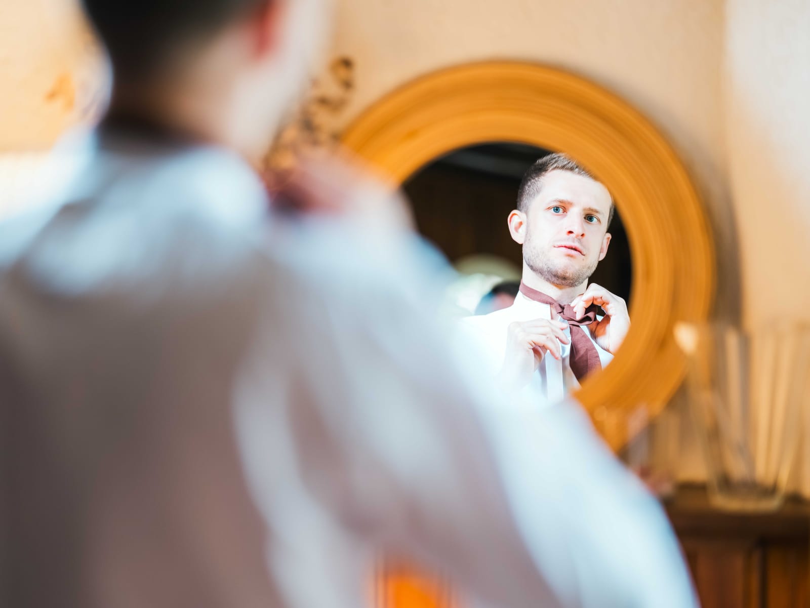 Jean-Baptiste ajuste sa tenue devant un miroir rond pendant ses préparatifs, mariage au Abbaye de Longpont & Paris, par Jean-Baptiste Argyre (Jaysphotography)