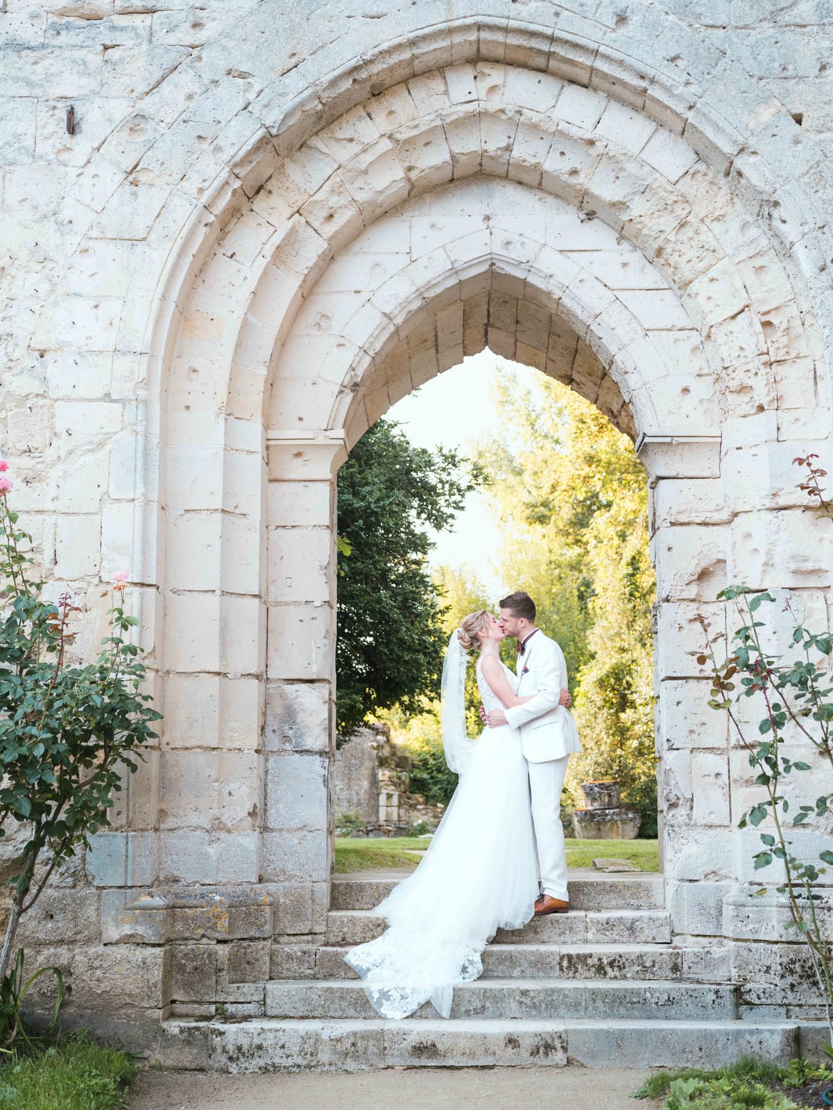 Mélanie et Jean-Baptiste s'embrassent sous une arche gothique de l'abbaye, sur les marches, mariage au Abbaye de Longpont & Paris, par Jean-Baptiste Argyre (Jaysphotography)
